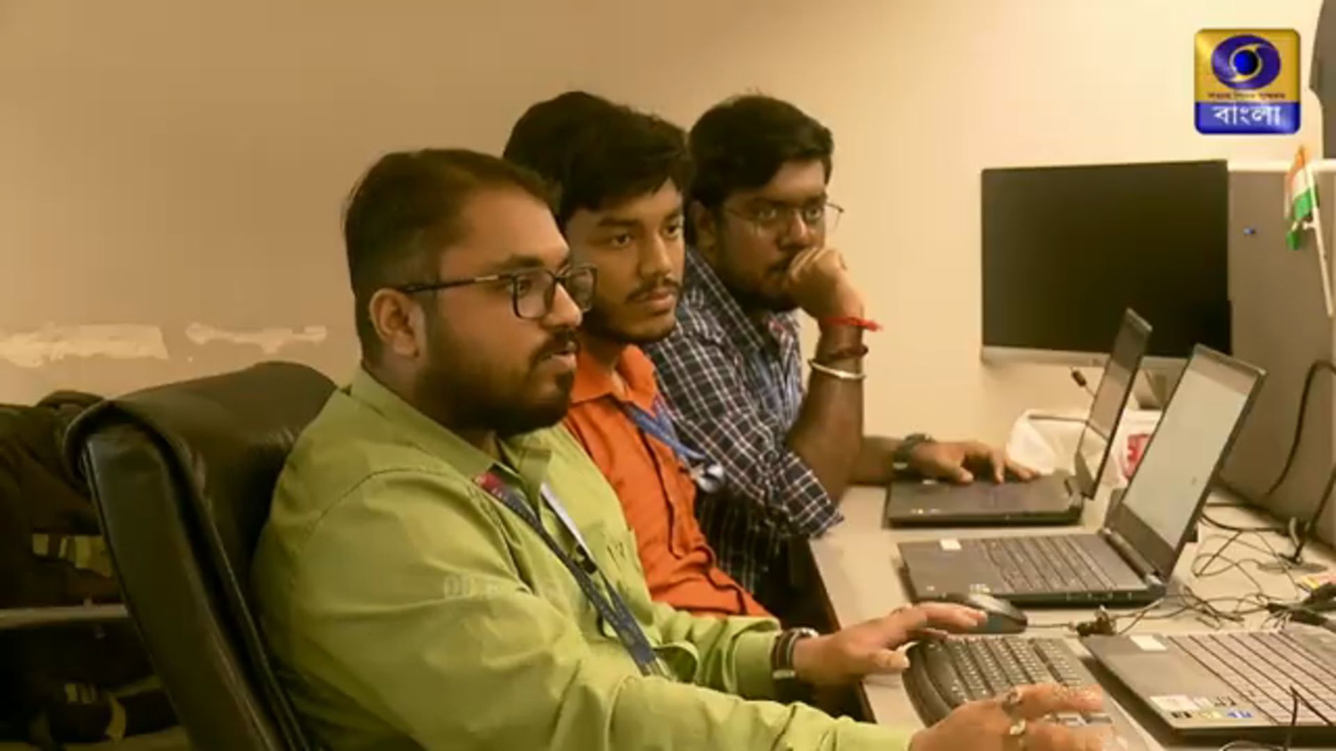 Still from the same sequence a moment later: the three colleagues continue working, the two furthest from camera watching a laptop screen.
