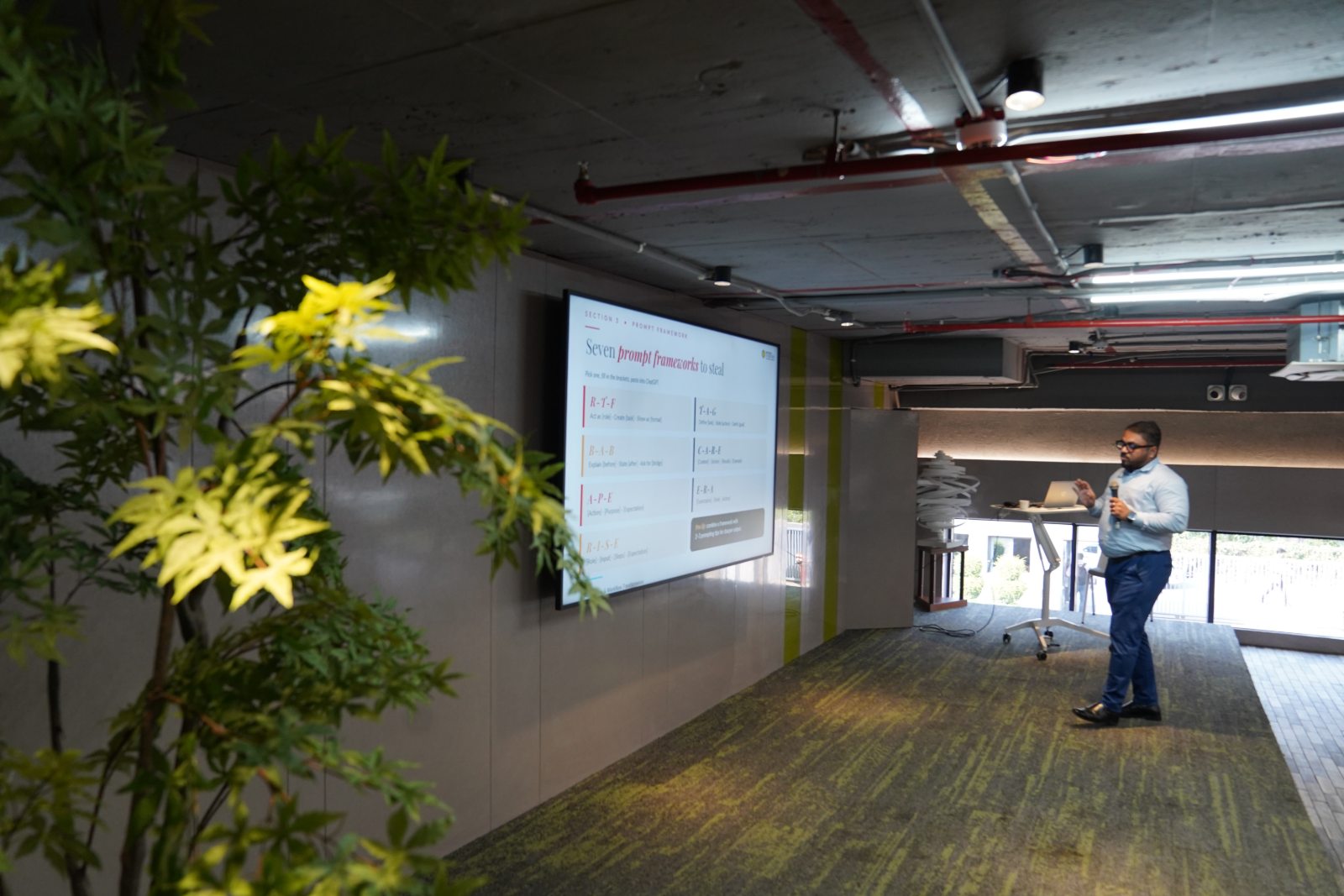 A wide view of the session space, the prompt-frameworks slide on the wall screen and Sourish Mukherjee presenting at the far end.